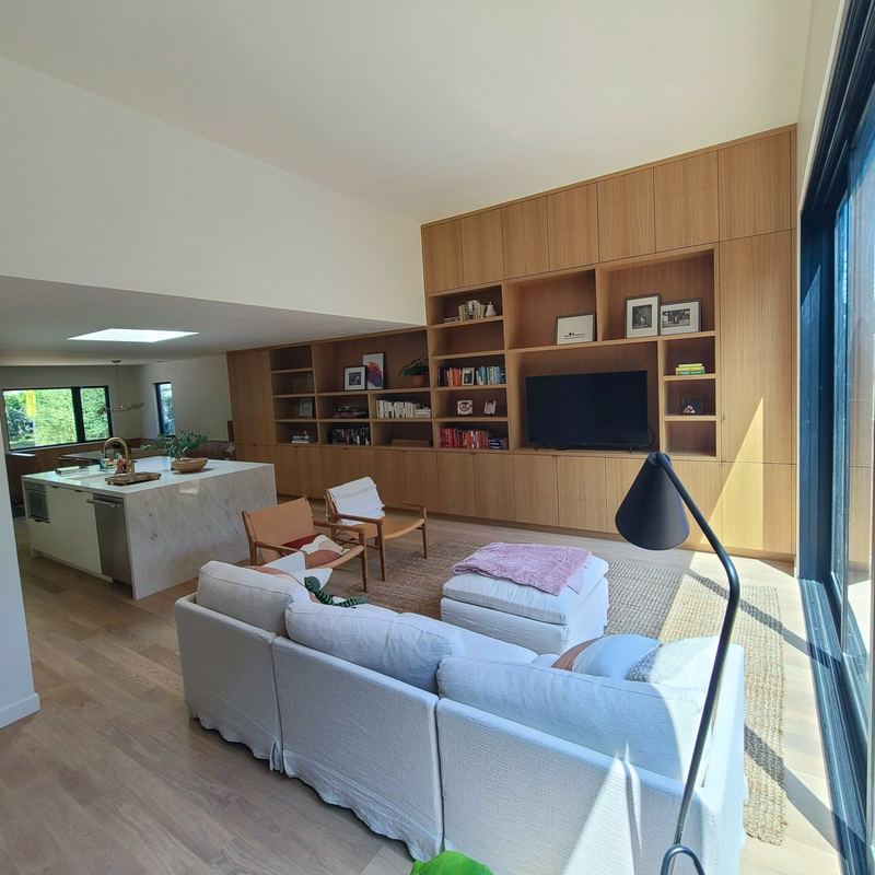 Open great room with a full wall of white oak built-in shelving and the marble kitchen island beyond