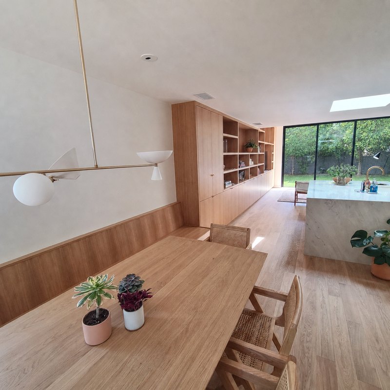 Dining area with long oak table, cane chairs, oak wall paneling, brass light fixture and skylight