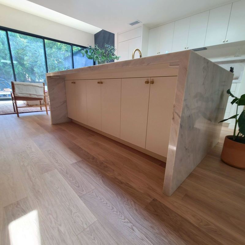 Kitchen island wrapped in mitered marble with pale cabinetry and brass hardware