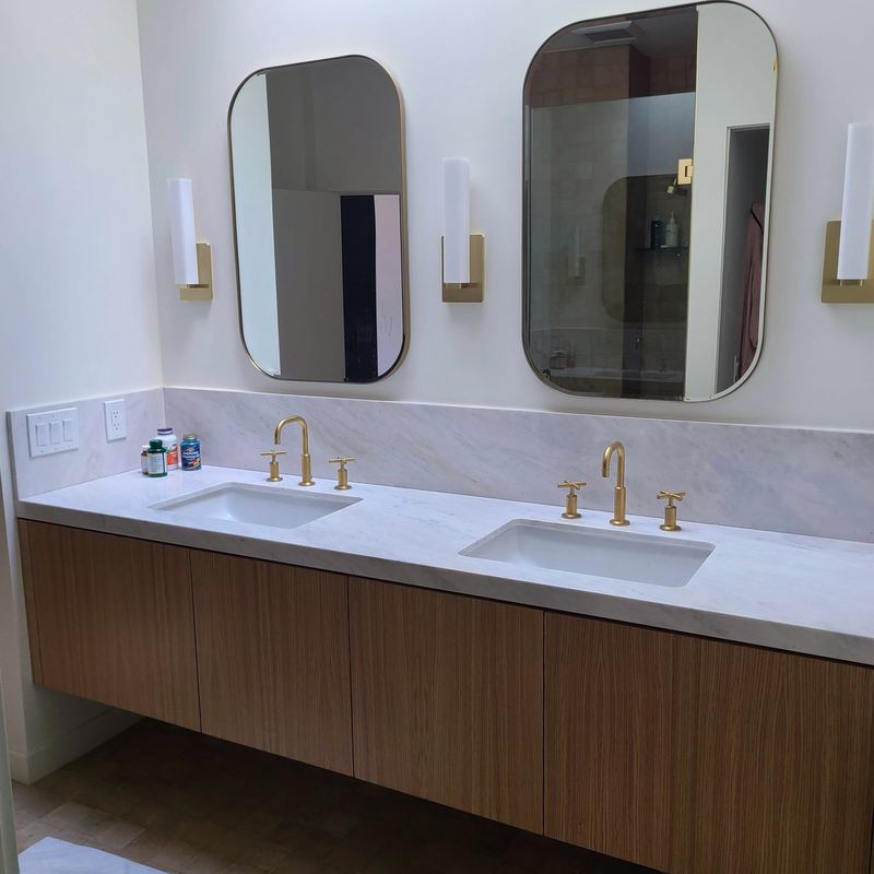 Primary bathroom double vanity in white oak with marble countertop, full marble backsplash and brass fixtures