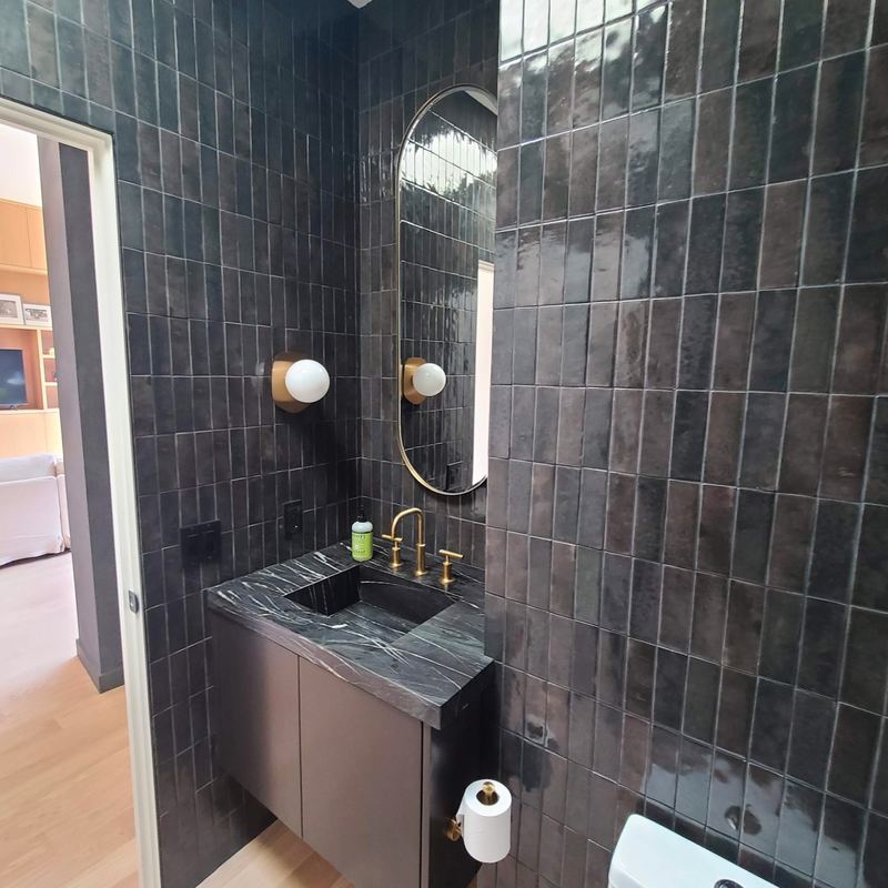 Powder room tiled floor to ceiling in glazed black zellige with a black marble vanity and brass fittings