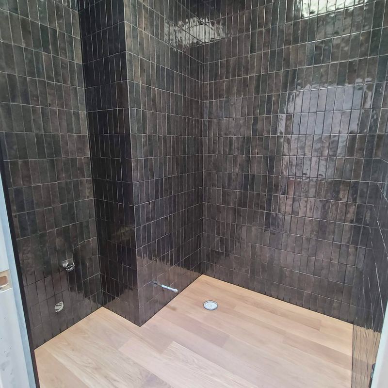 Shower enclosure tiled in dark hand-glazed tile during construction