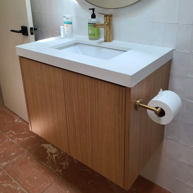 Floating white oak vanity with a thick white quartz countertop and brass fixtures over terracotta tile