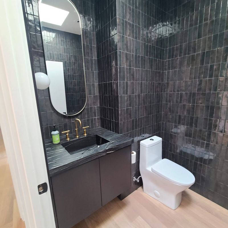 Dark vanity with black marble countertop, integrated sink and brass widespread faucet against black zellige tile